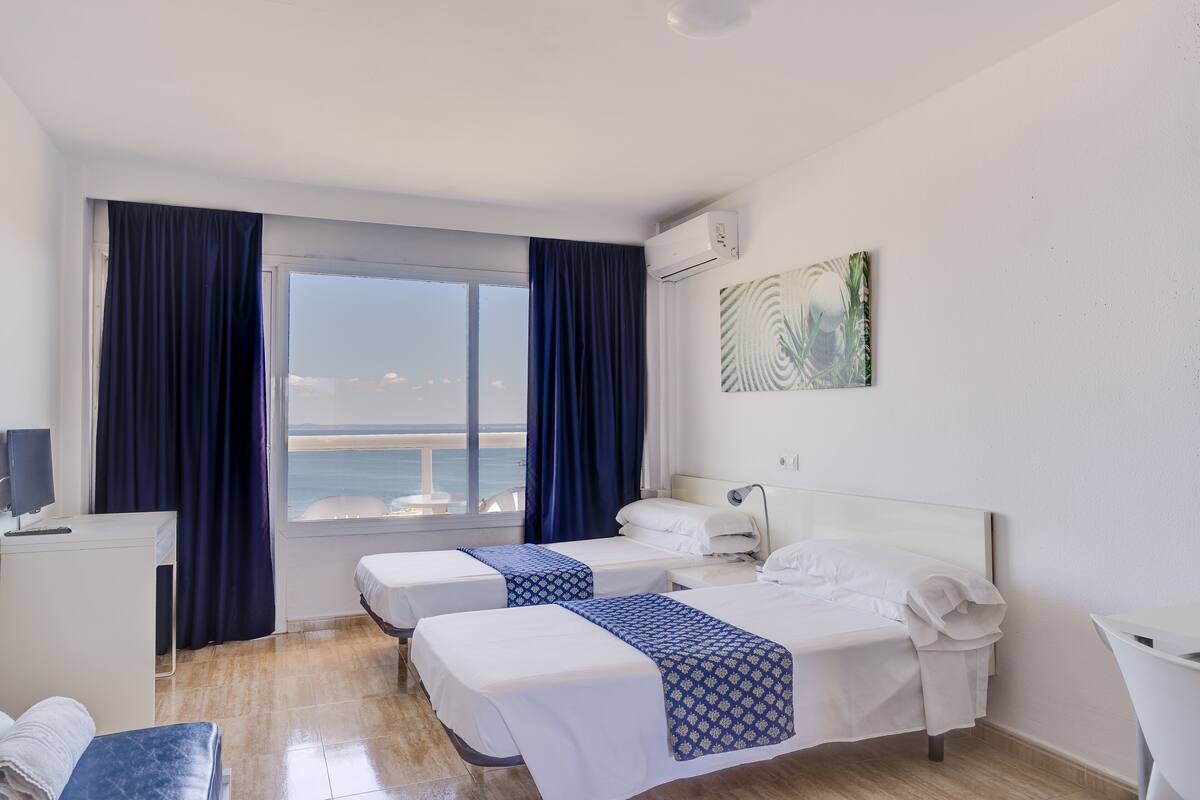 Ein Hotelzimmer mit zwei Betten, einem Schreibtisch, einem Stuhl, einem Fernseher und einem Fenster mit Vorhängen.