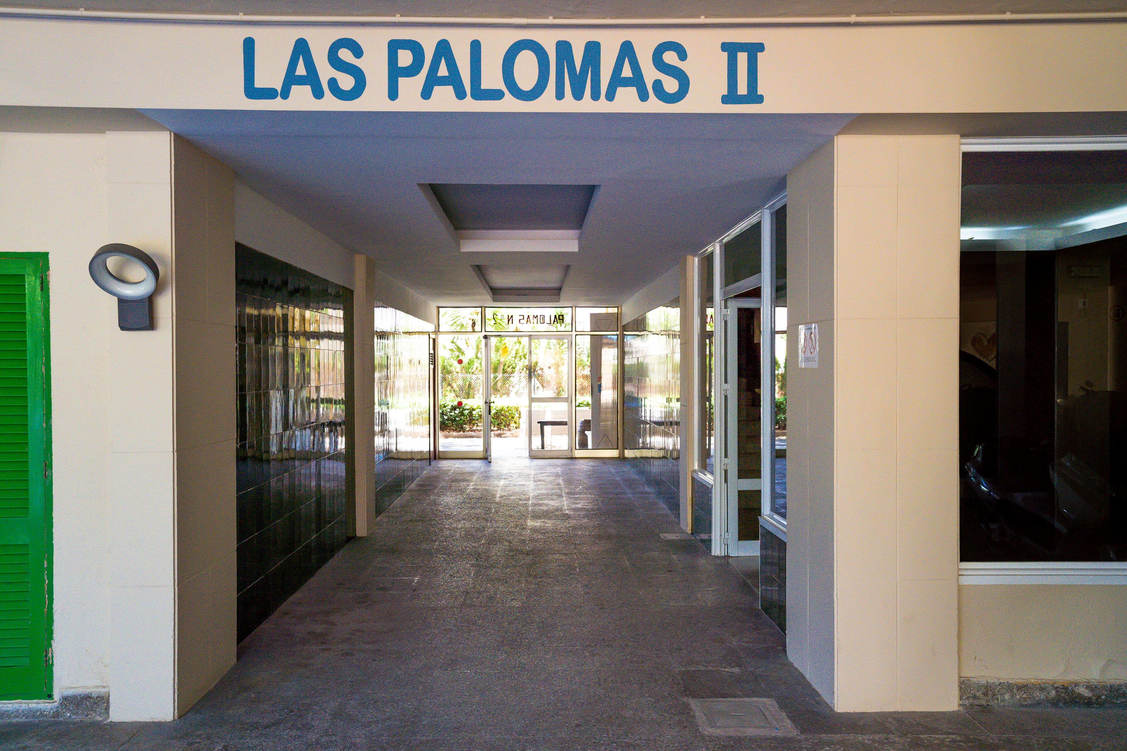 Un pasillo que conduce a la entrada de un edificio, con un letrero que dice 'LAS PALOMAS II'.