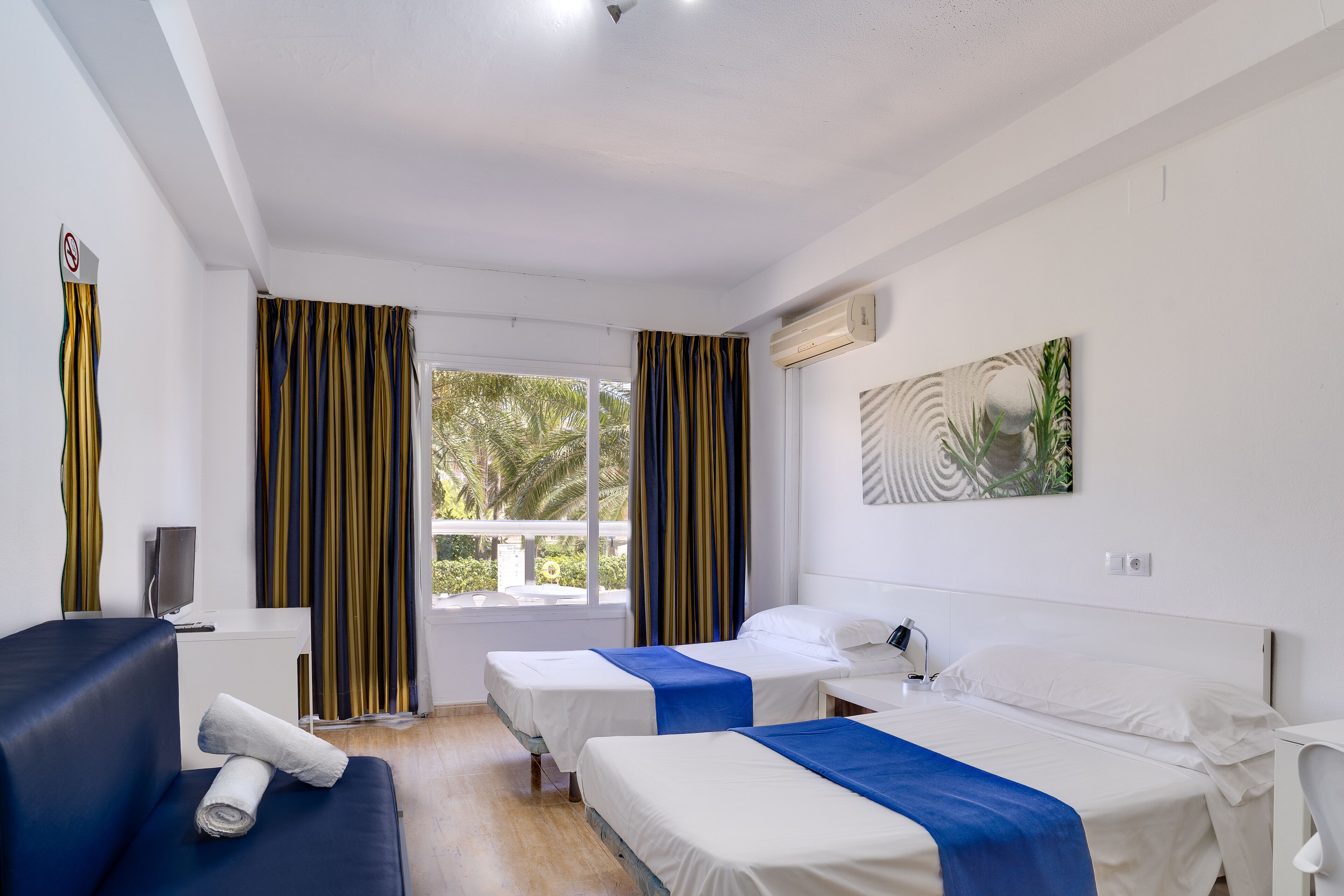 A hotel room with two beds, a desk, a chair, a TV, and a window with curtains.