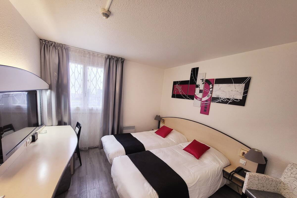 Habitación de hotel con dos camas, un escritorio, una silla y un televisor.