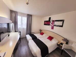 A hotel room with two beds, a desk, a chair, and a TV.