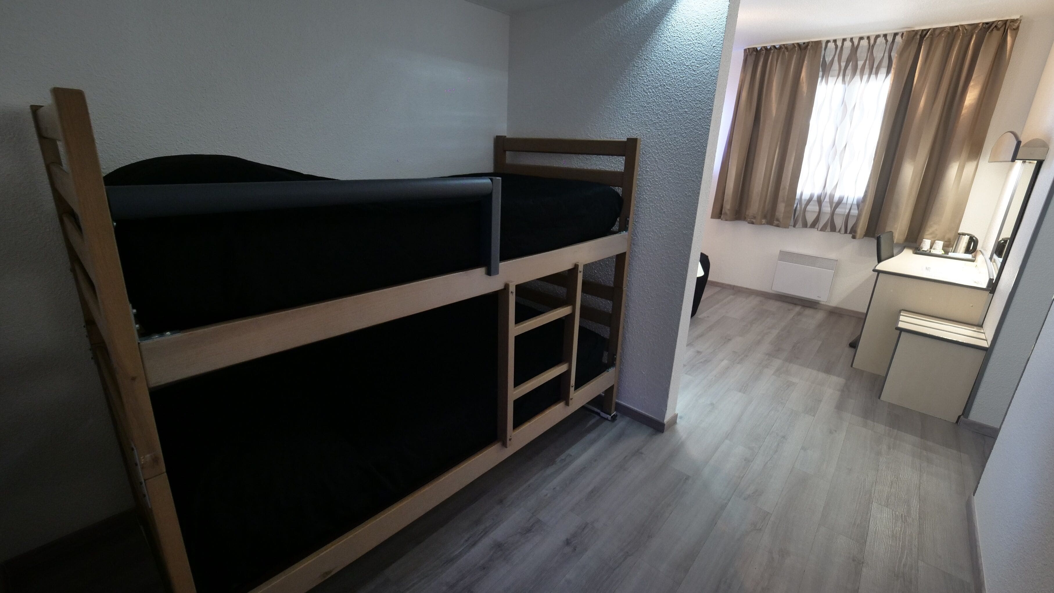Una cama litera con escritorio y espejo en una habitación pequeña.