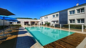 A swimming pool with sun loungers and umbrellas, surrounded by a building with large windows and a white exterior.