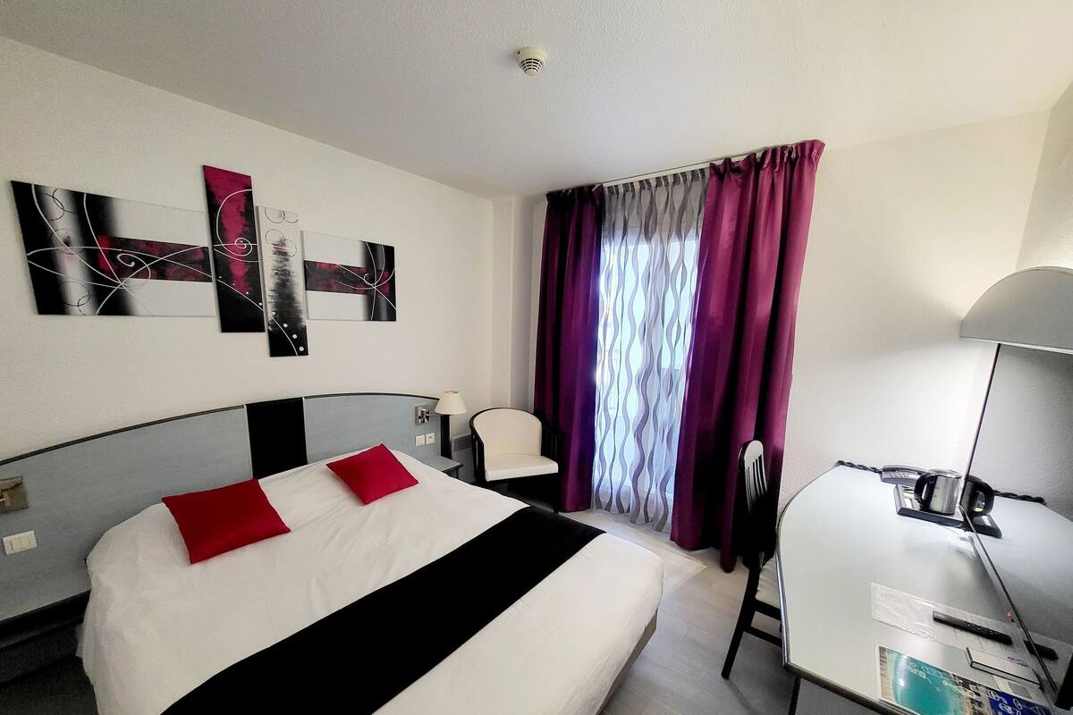 Habitación de hotel con cama, escritorio, silla y televisor.