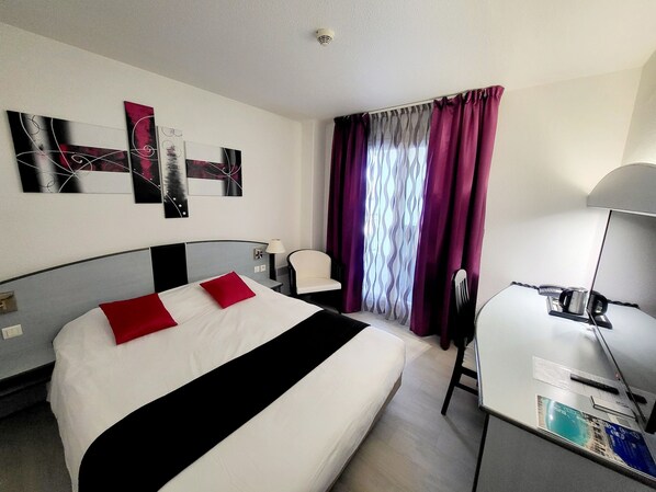A hotel room with a bed, a desk, a chair, and a TV.