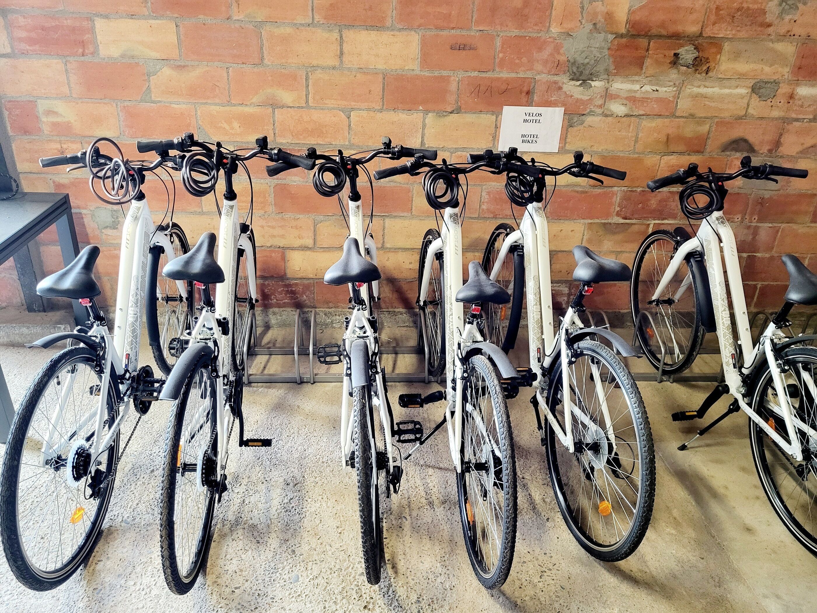 Una fila de bicicletas estacionadas contra una pared de ladrillo, con un letrero que indica 'VELOS HOTEL' encima.