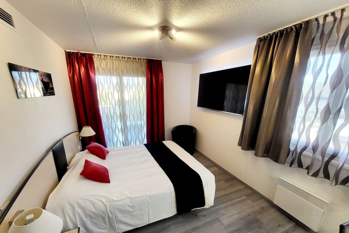 Una habitación de hotel con cama, televisión, escritorio y ventana con cortinas.