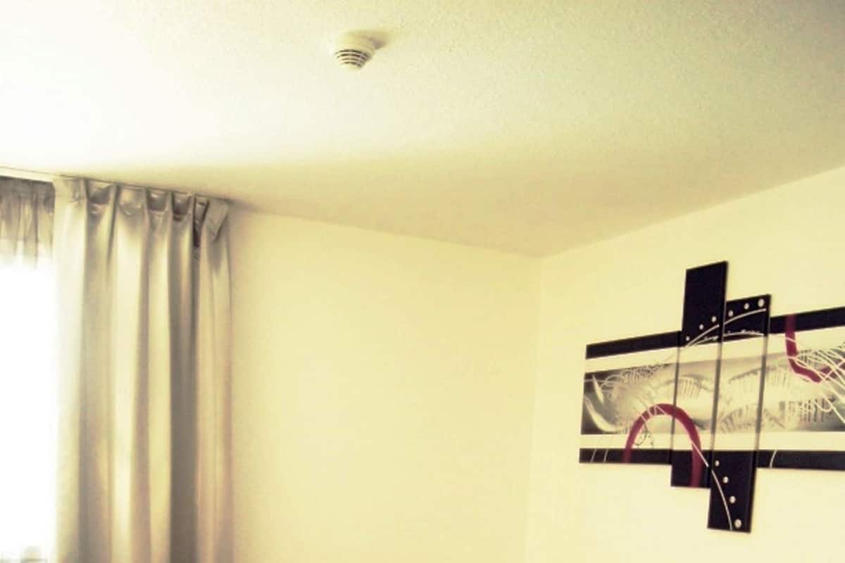 Habitación de hotel con cama, mesita de noche, lámpara, ventana con cortinas y una obra de arte en la pared.