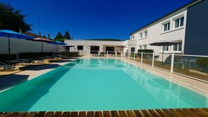 A swimming pool with lounge chairs and umbrellas, surrounded by a white building with multiple windows.