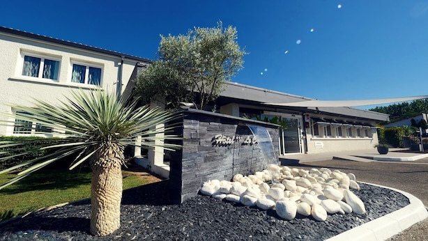 A hotel with a stone facade, a palm tree, and a landscaped area with white stones.