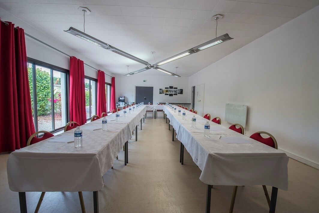 A conference room with long tables, red curtains, and ceiling fans.