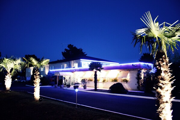 A hotel with a well-lit facade, palm trees, and a clear night sky.