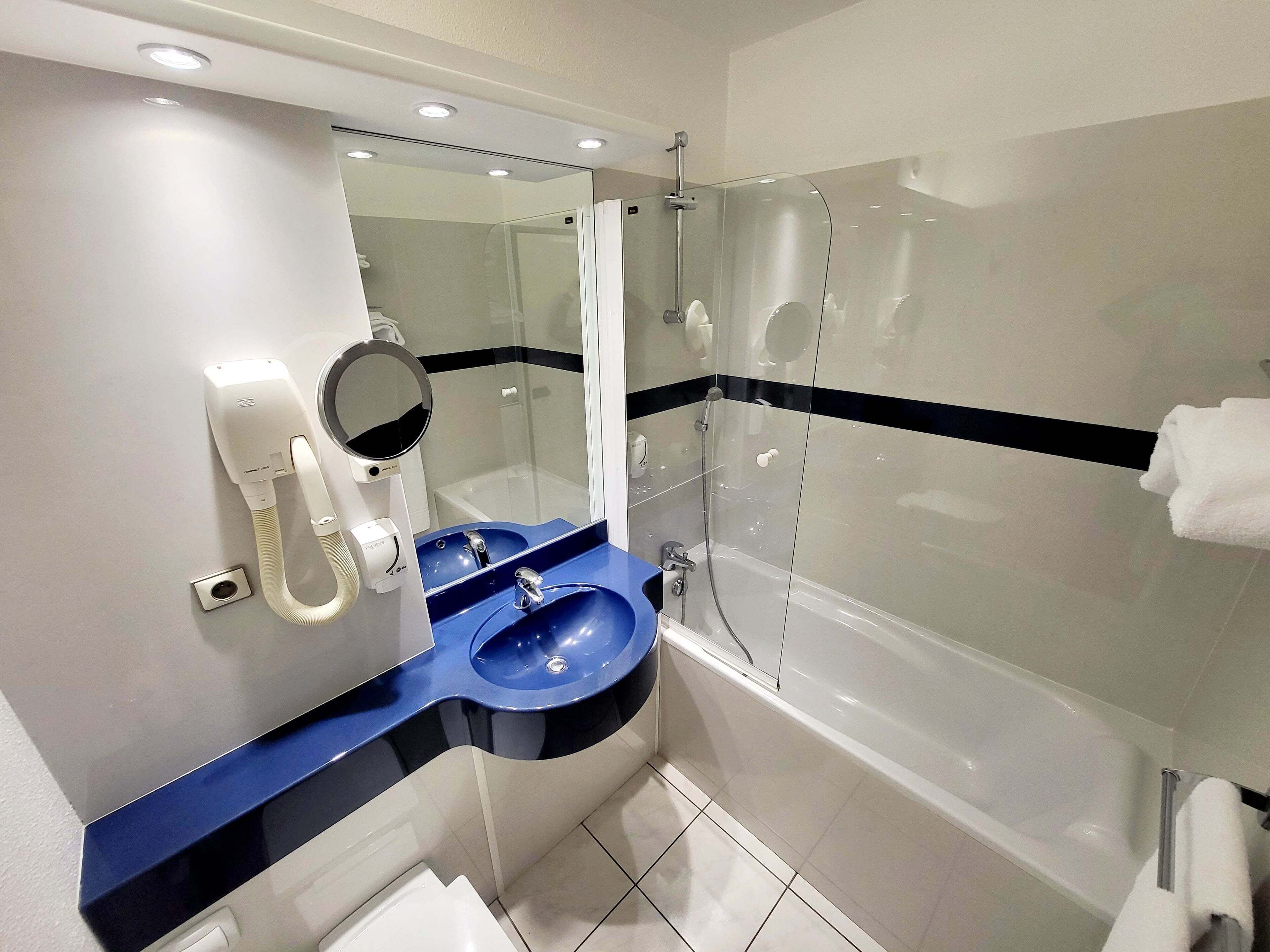 Un baño moderno con un lavamanos azul, un espejo, un cabezal de ducha de mano y una bañera.