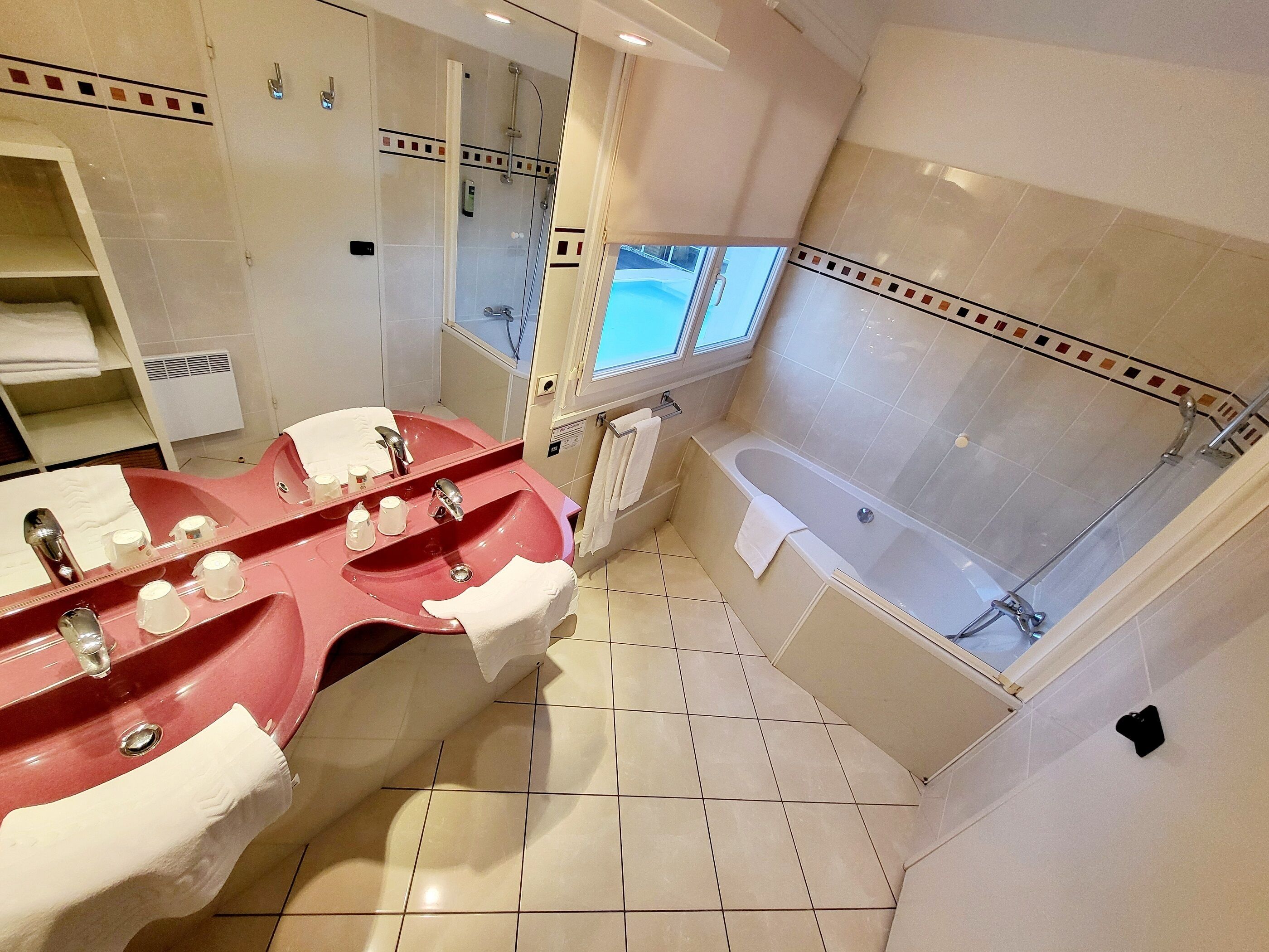 Un baño moderno con una bañera grande, un lavabo doble con un lavamanos rojo y un espejo amplio.