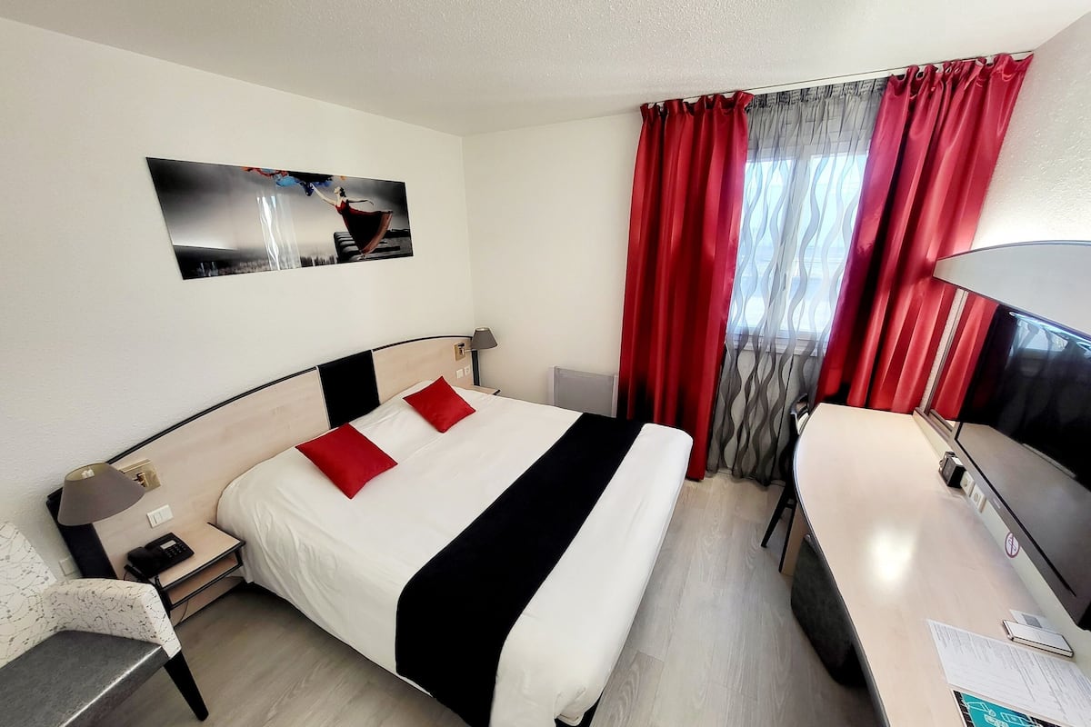 Una habitación de hotel con cama, mesita de noche, lámpara y escritorio con silla.