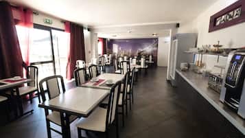 Un restaurante con varias mesas y sillas, una barra con máquina de café y un mural en la pared.
