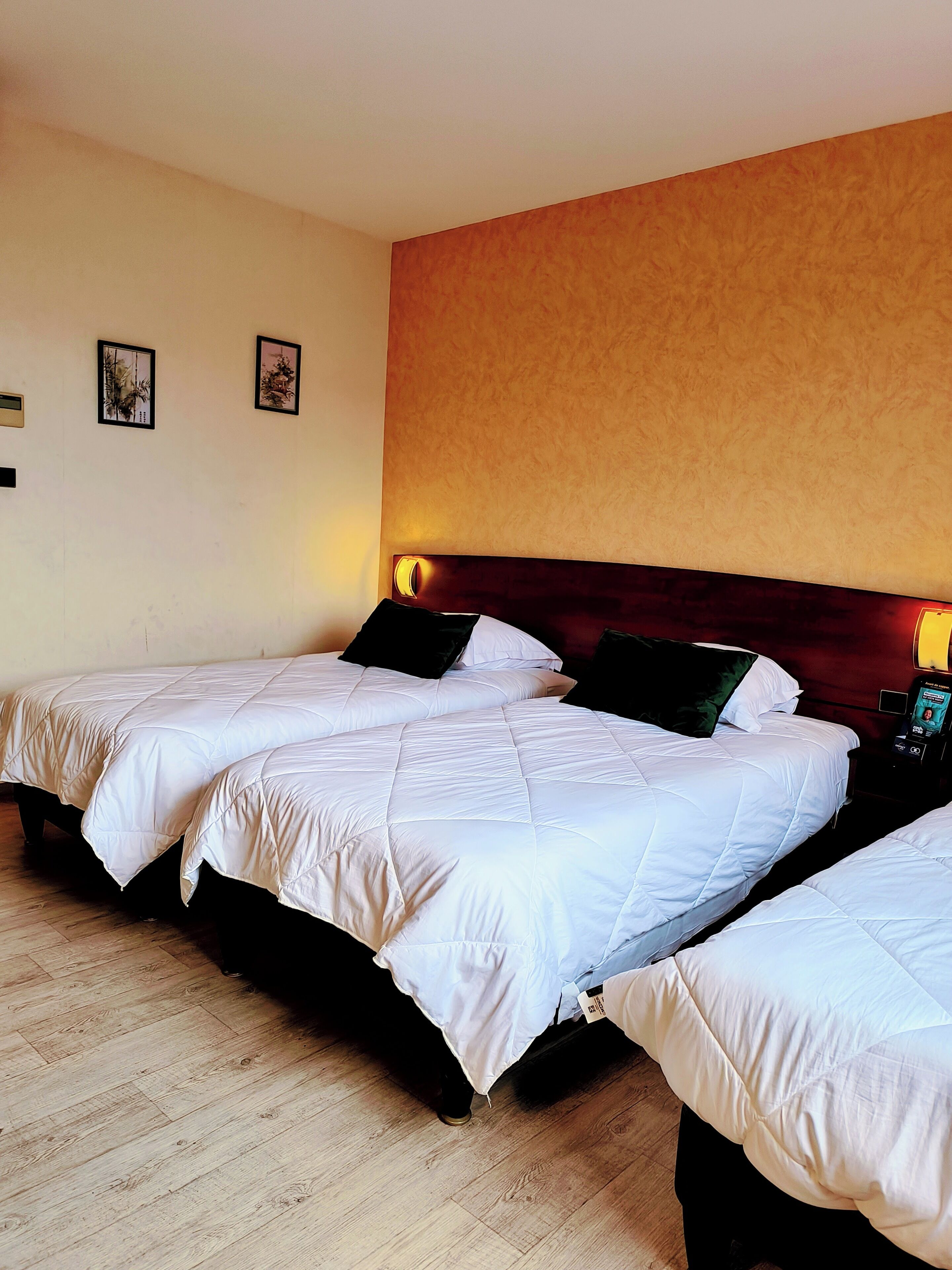 A hotel room with three beds, wooden flooring, and a wooden headboard.