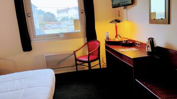 Habitación de hotel con cama, escritorio, silla, televisor y ventana con vista a edificios.
