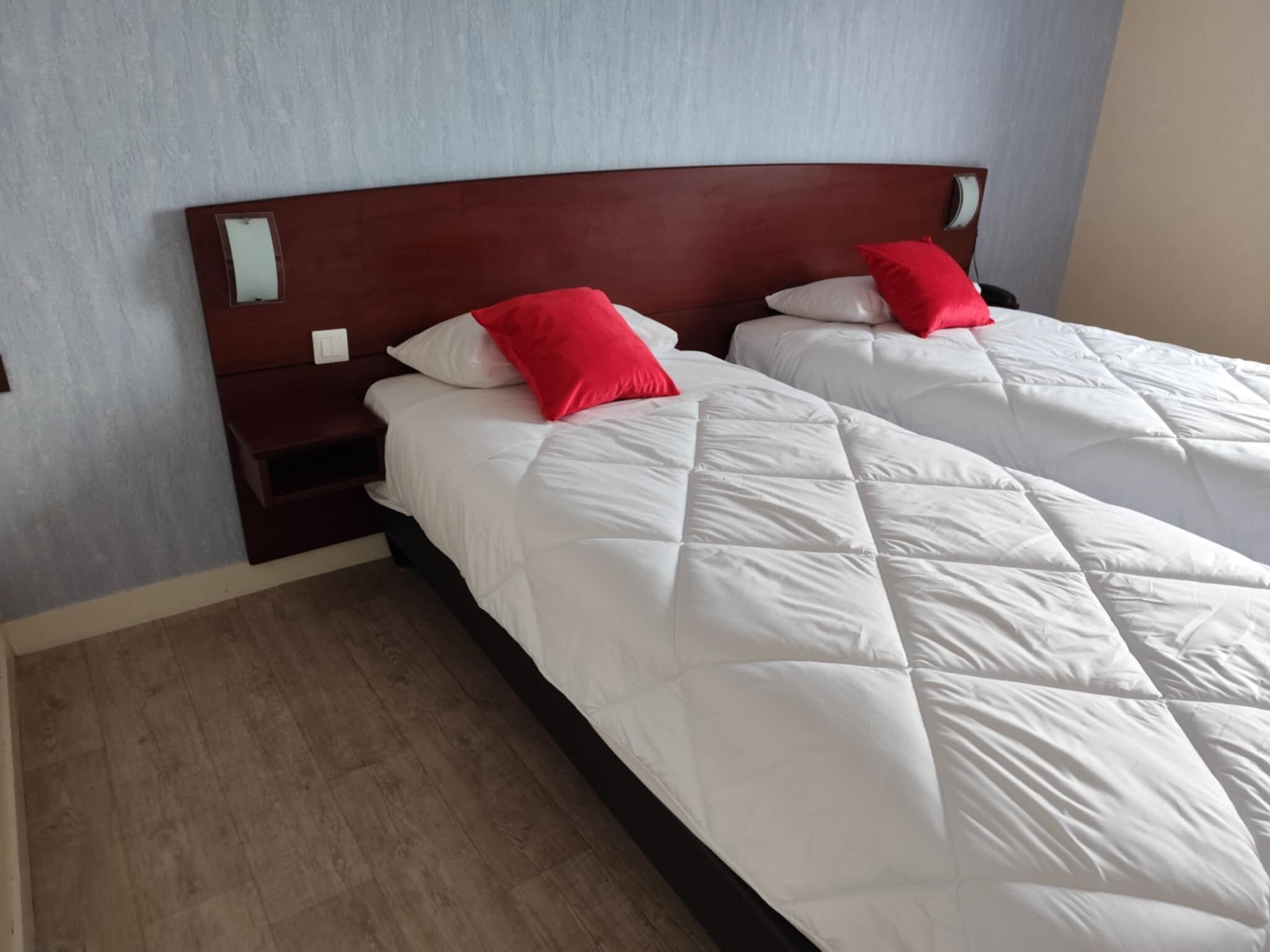 Une chambre d’hôtel avec deux lits simples, chacun doté d’une tête de lit en bois et de linge de lit blanc.