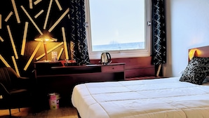 A modern bedroom with a large bed, a desk with a lamp, and a view through a window. - Hotel Saint Jacques (Parthenay)