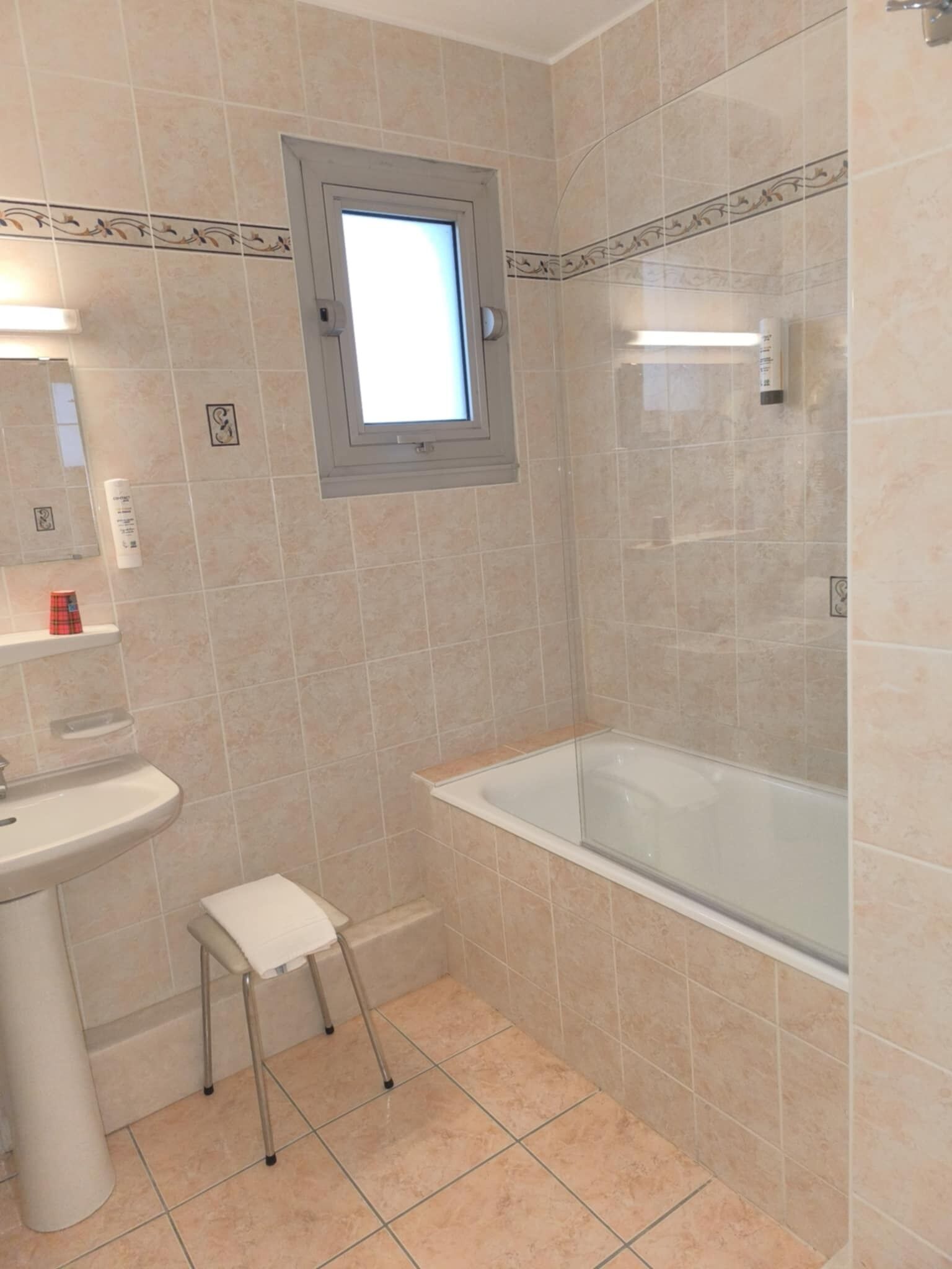 Un baño con bañera, lavamanos y un taburete pequeño.