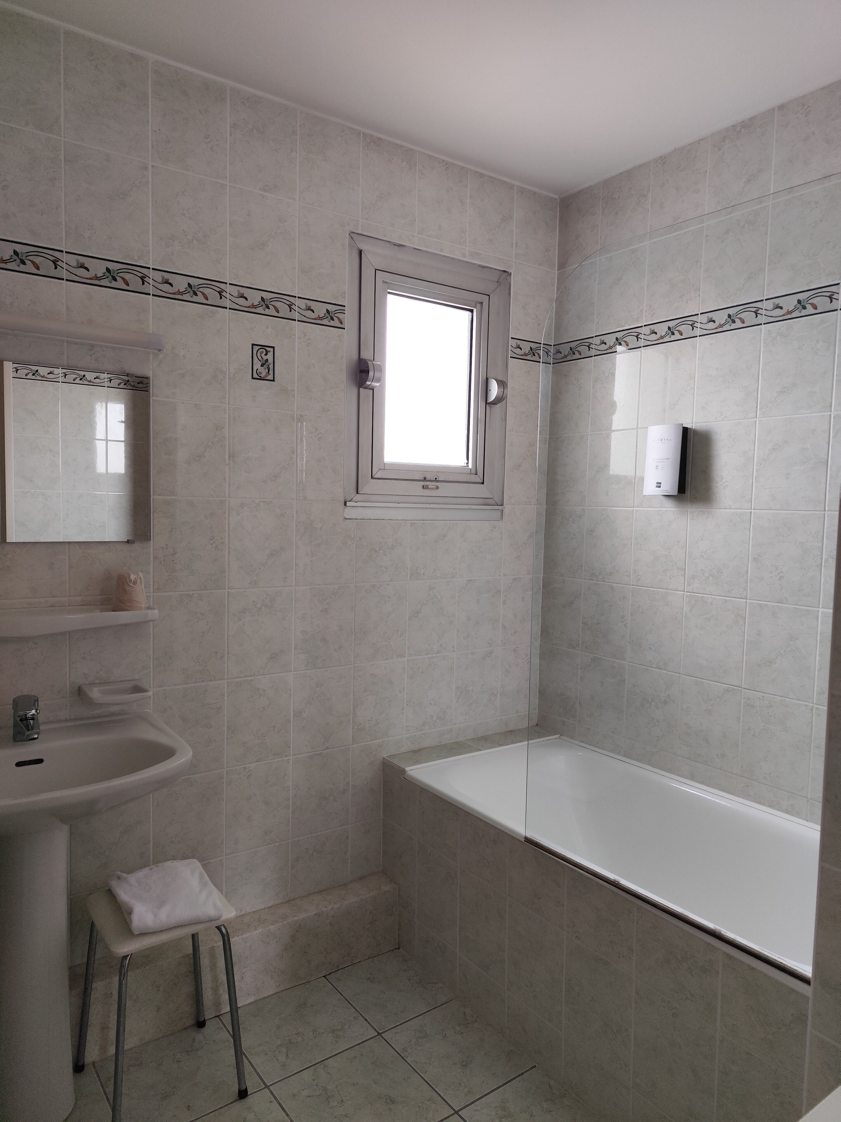 A bathroom with a bathtub, a sink, a window, and a mirror.