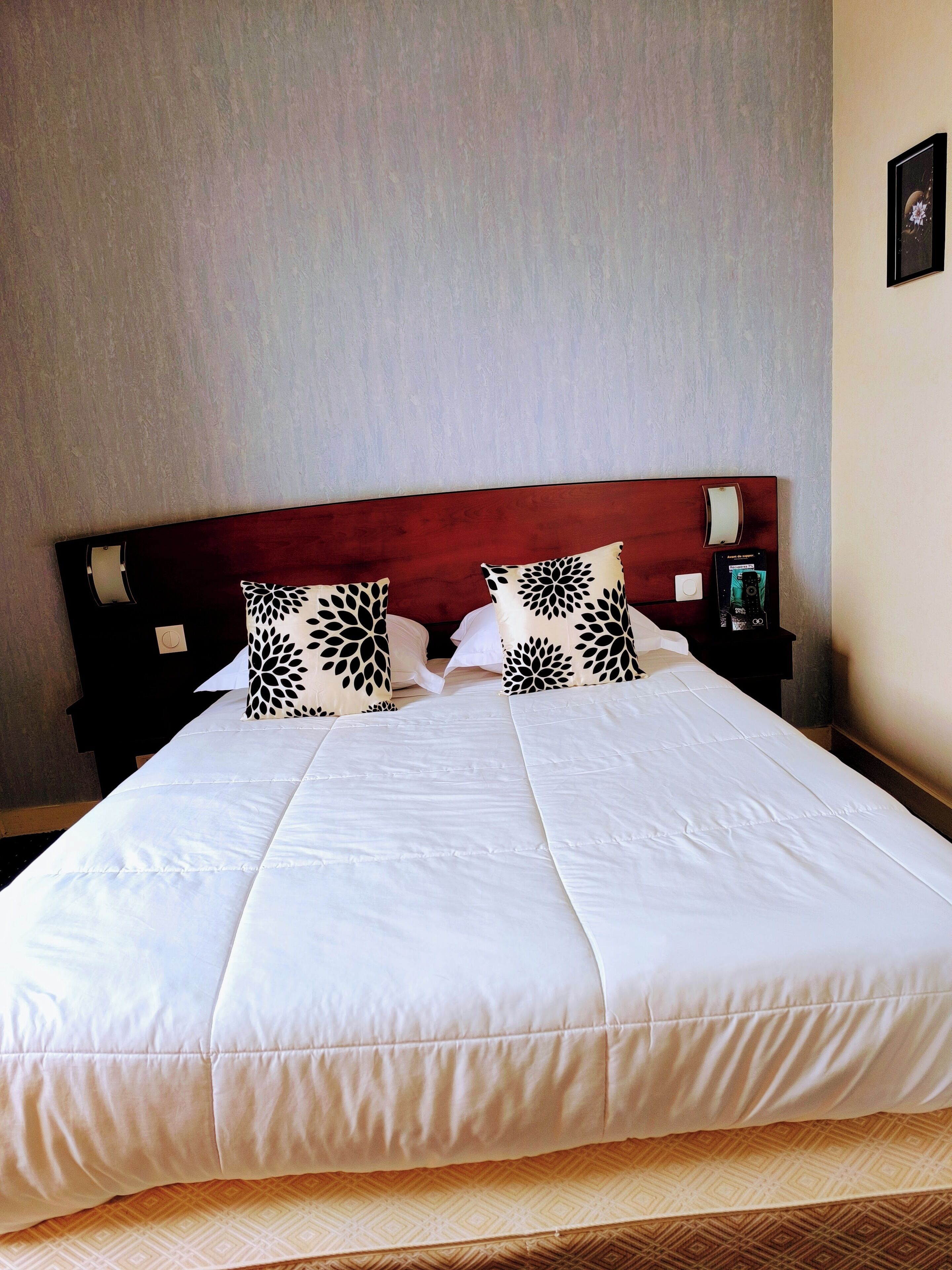 A neatly made bed with white bedding and two decorative pillows with a black leaf pattern.