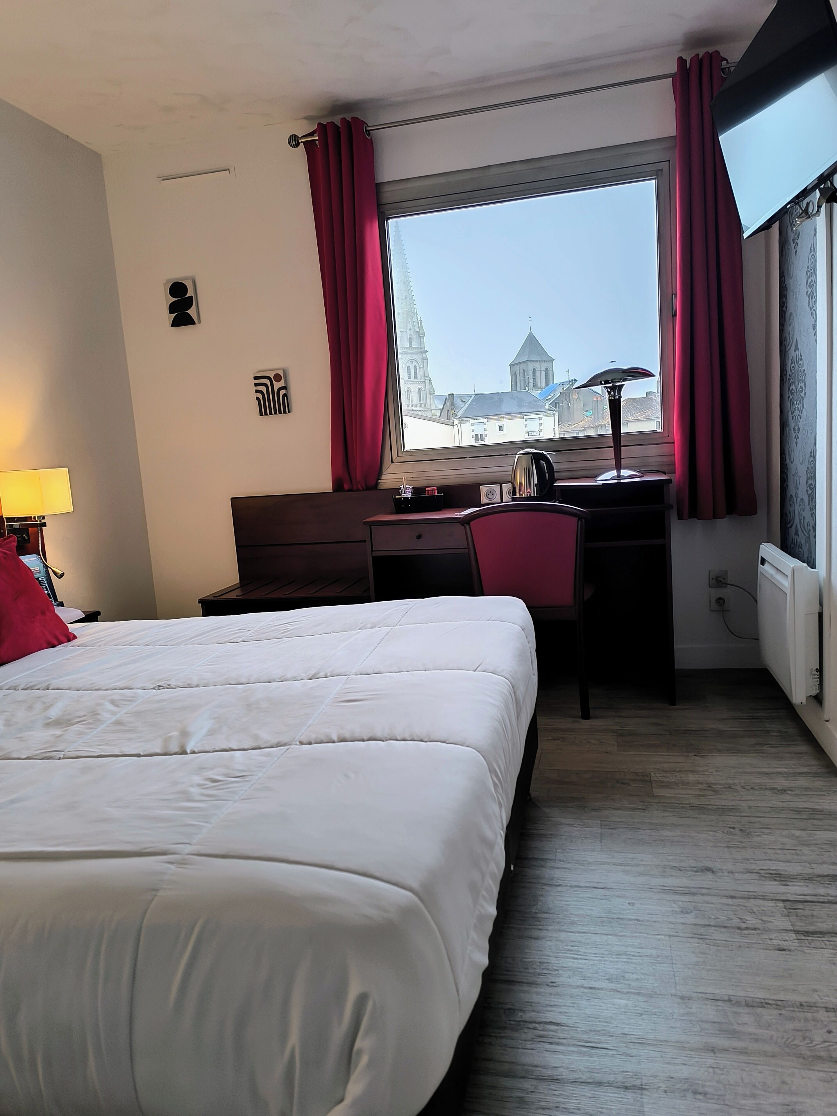 Habitación de hotel con una cama grande, un escritorio, una silla y una ventana que ofrece vistas a un edificio.