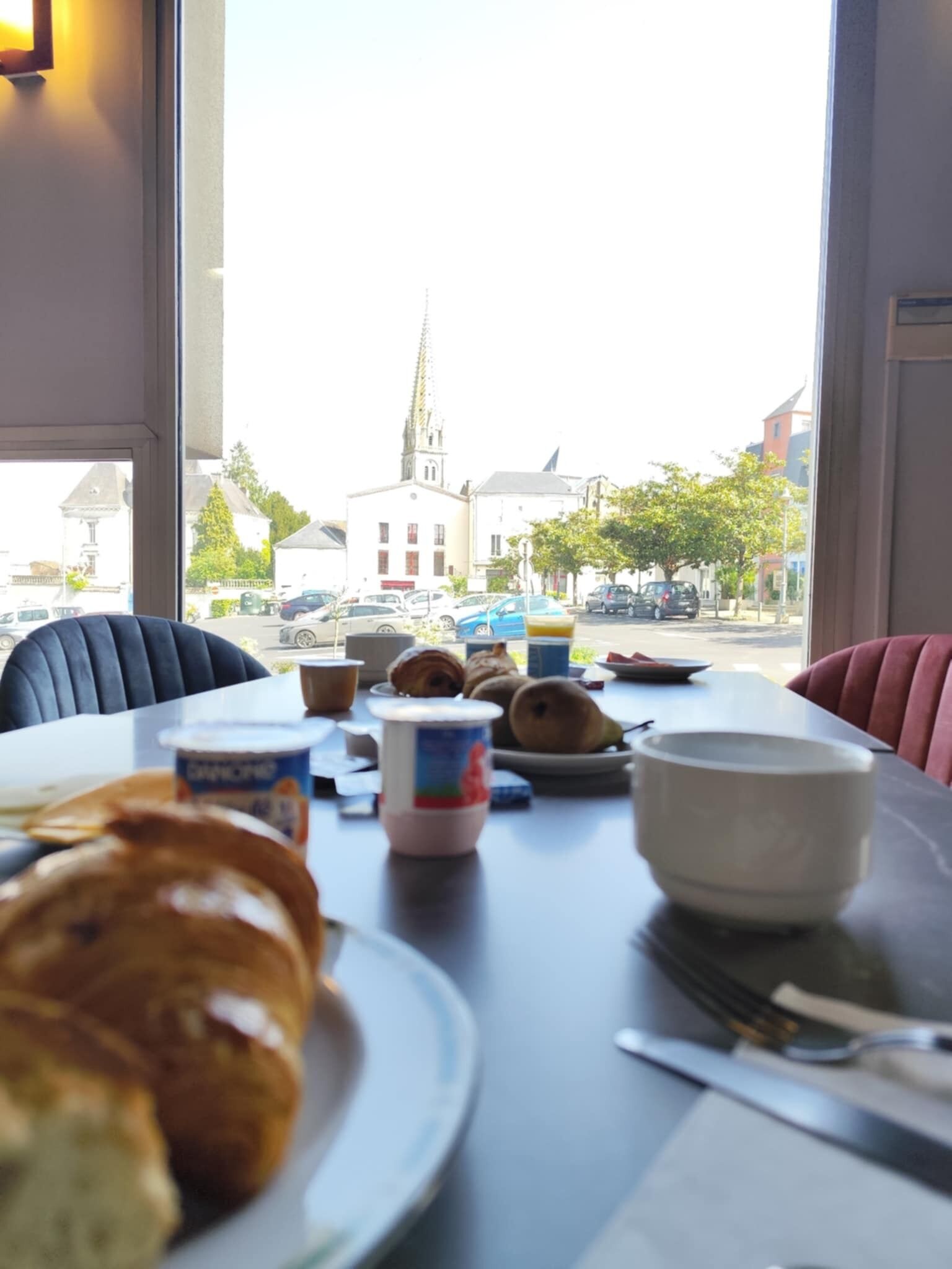 A dining table with pastries and a cup of coffee, a window with a view of a church and buildings, and a chair.
