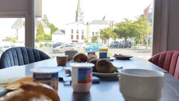 A dining table with pastries and a cup of coffee, a window with a view of a church and buildings, and a chair.