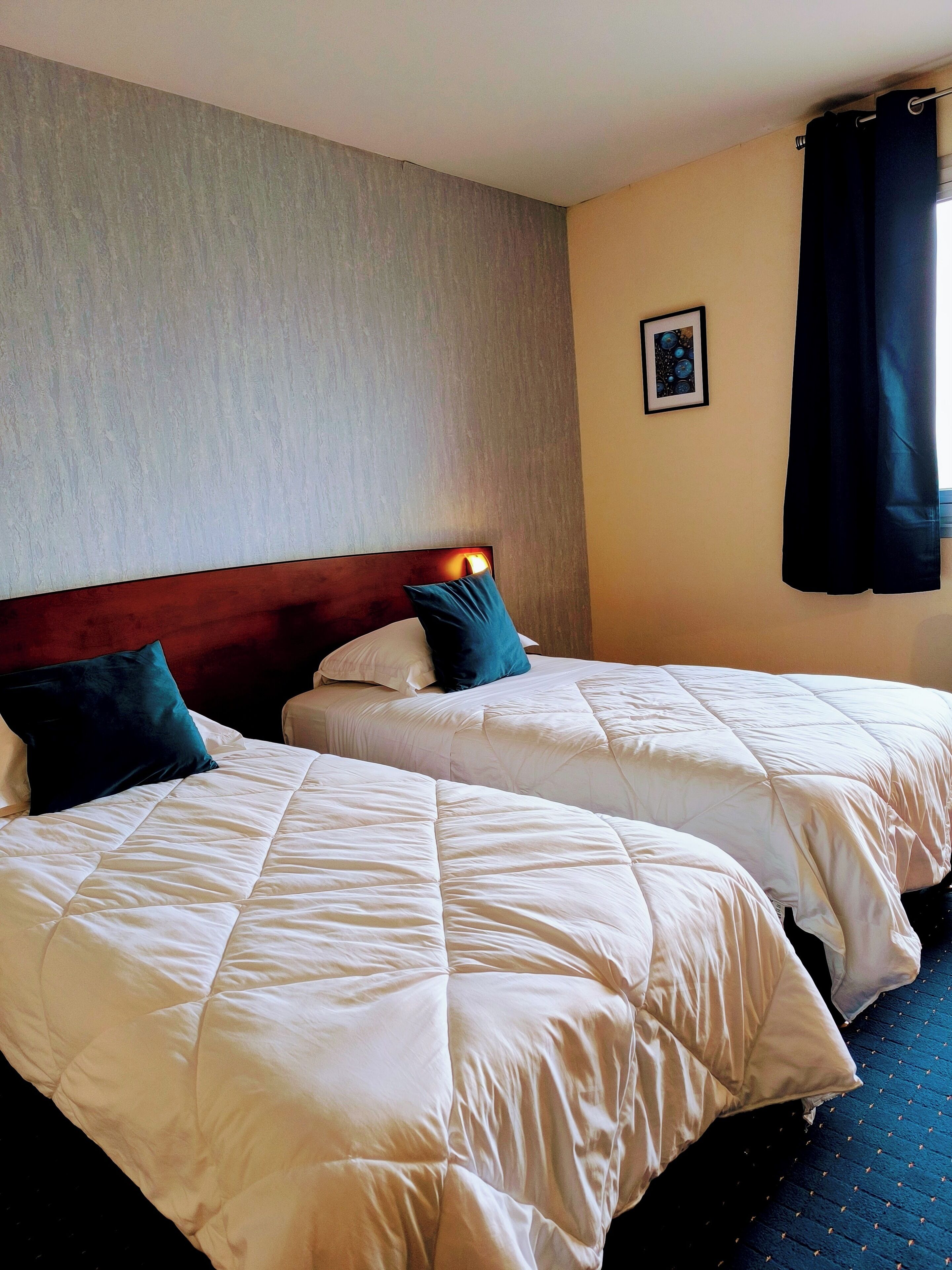 Quarto de hotel com duas camas, cada uma com roupa de cama branca e almofadas azuis.