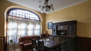 A dining room with a wooden table, chairs, a sofa, and a large window with curtains. - Casa España (Villaviciosa)