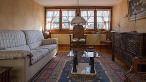 A living room with a sofa, a glass coffee table, a patterned rug, a wooden cabinet, and a painting on the wall. - Casa España (Villaviciosa)
