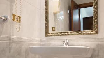Un baño con un lavabo pedestal, un espejo con marco ornamentado y un secador de pelo montado en la pared.