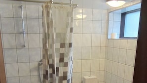 Et badeværelse med bruser, toilet og et vindue.