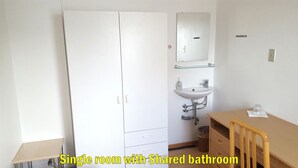 Et enkelt værelse med fælles badeværelse, med garderobe, håndvask og lille bord.