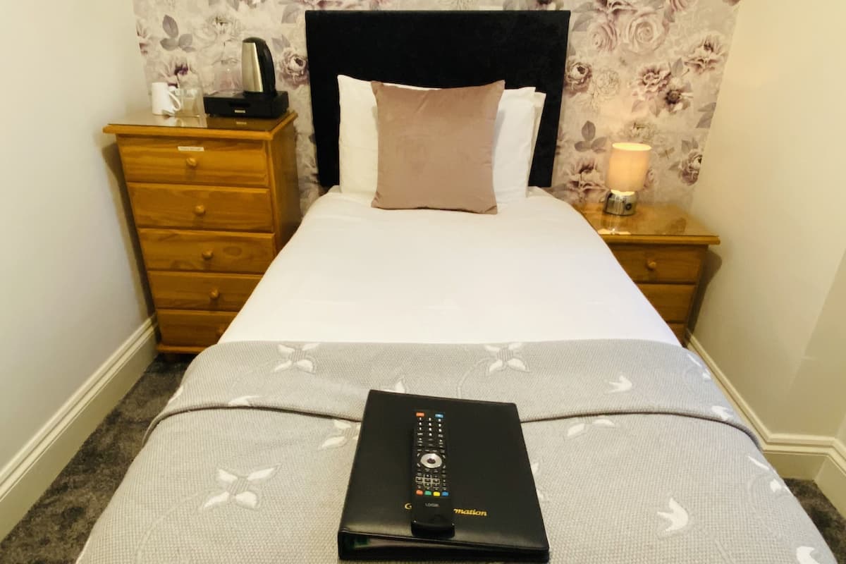 A neatly made bed with a floral wallpaper, a bedside lamp, and a remote control on the bed.