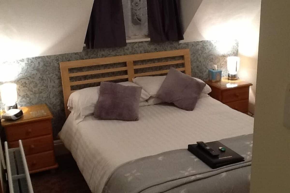 A neatly made bed with two pillows, a wooden headboard, and a bedside table with a lamp.
