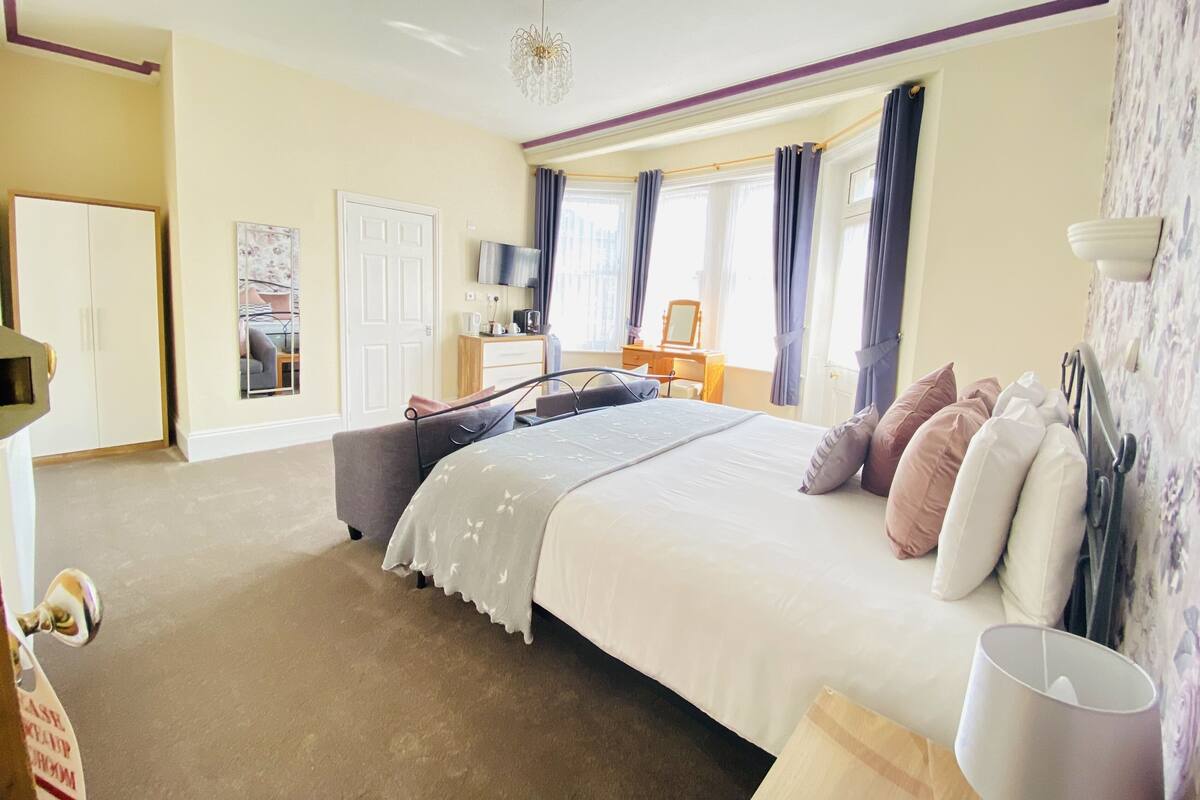 A bedroom with a large bed, a dresser, a desk, and a chair.