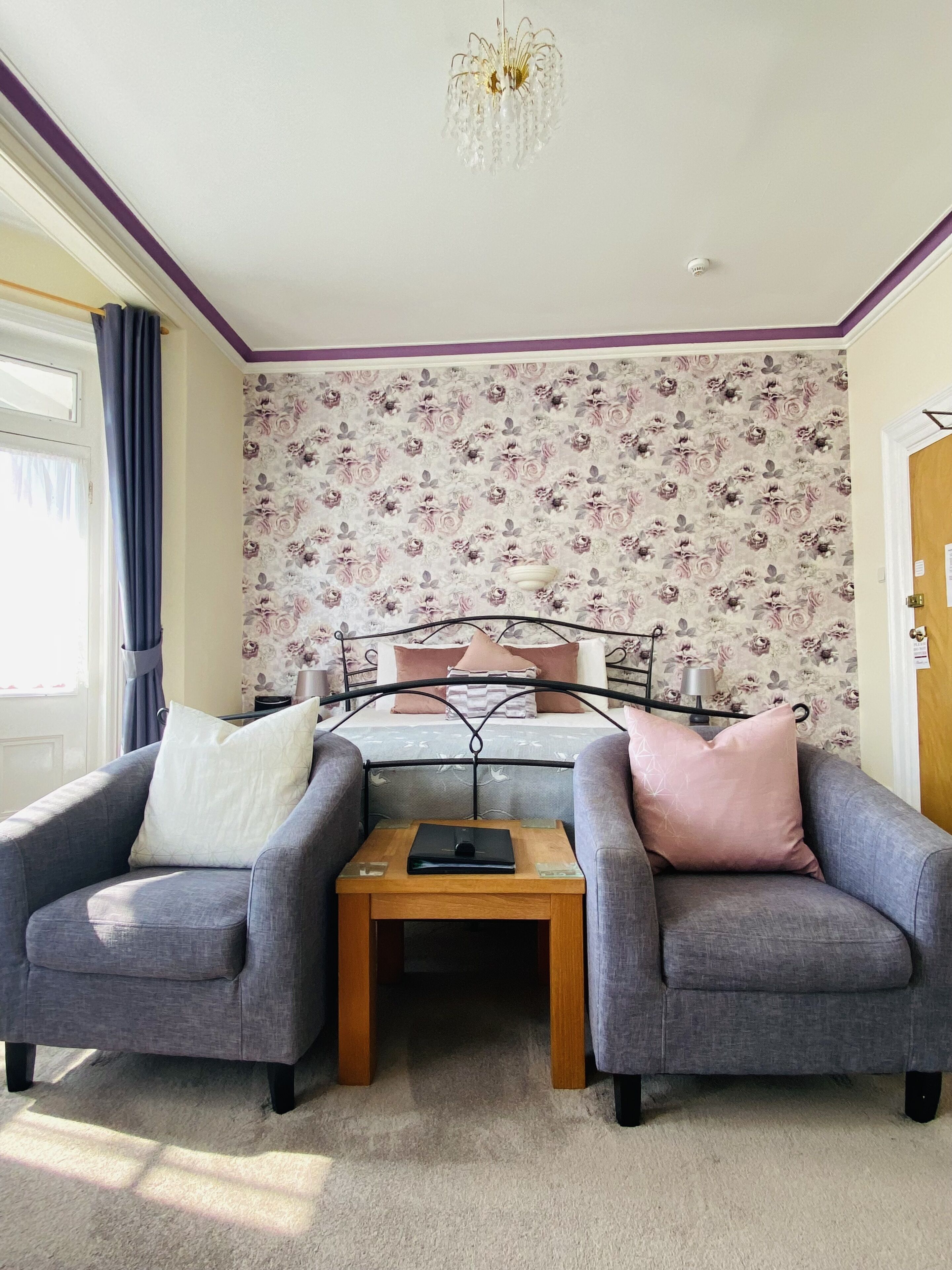 Ein Zimmer mit einem Bett, zwei Sesseln, einem kleinen Tisch und einer Deckenleuchte.