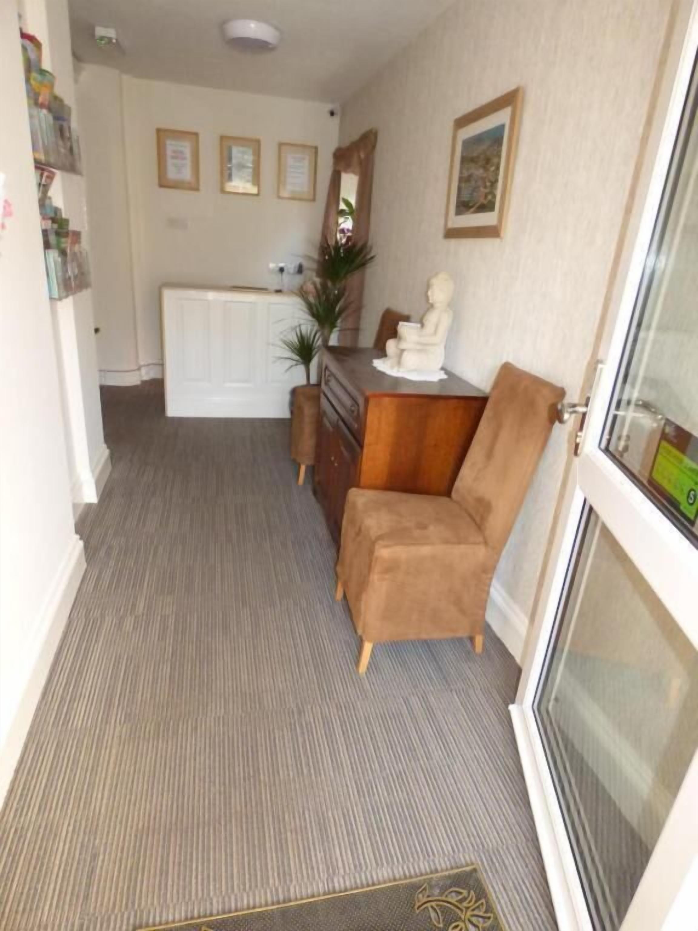 A compact living space with a kitchenette, a wooden cabinet, a plush armchair, and a radiator.