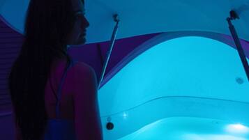 A person seated inside a bathtub with a curved ceiling and a blue light.