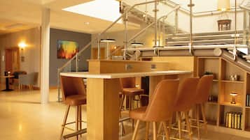 A modern bar area with a wooden bar counter and leather bar stools.