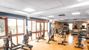 A gym with various exercise equipment, large windows, and a clock on the wall.