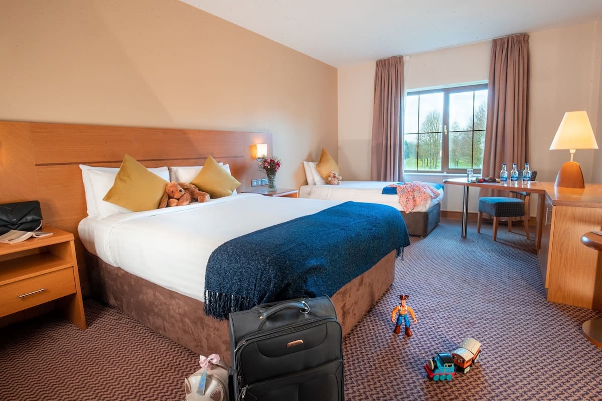 A hotel room with two beds, a desk, a chair, a TV, and a window with curtains.