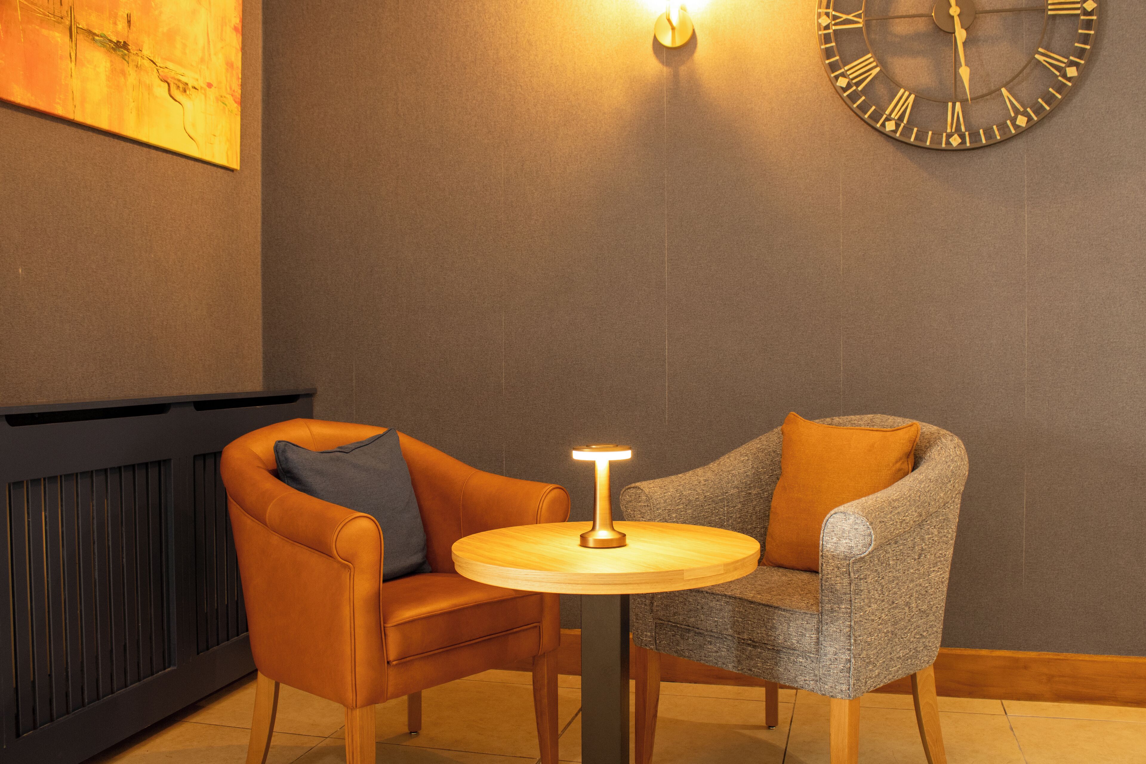 A modern room with two chairs, a round table, a wall clock, and a painting.