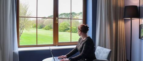 Una habitación con un ventanal grande, una laptop sobre una mesita, una silla y una lámpara de pie.