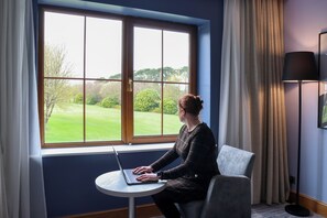 Une pièce avec une grande fenêtre, un ordinateur portable posé sur une petite table, une chaise et un lampadaire.