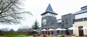 Un bâtiment en pierre doté d’une tour, des tables à l’extérieur avec des parasols et une clôture en bois.