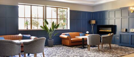 A modern living room with a blue accent wall, a fireplace, a large window, and a seating area with a table and chairs.